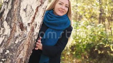 在阳光明媚的日子里，美丽的年轻金发女子在秋天多姿的公园里，微笑着欣赏秋天的树叶。 慢动作